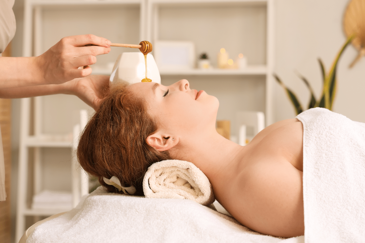 bienfaits miel peau Thérapeute qui verse du miel sur le visage d'une femme au salon de spa